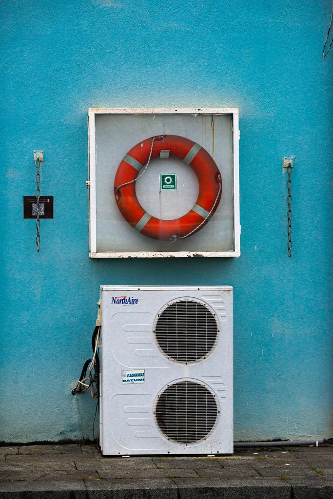 Outdoor wall with a lifebuoy and air conditioning unit on a bright blue background.